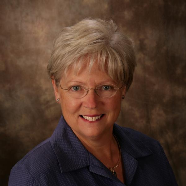 Smiling woman in glasses and purple shirt.