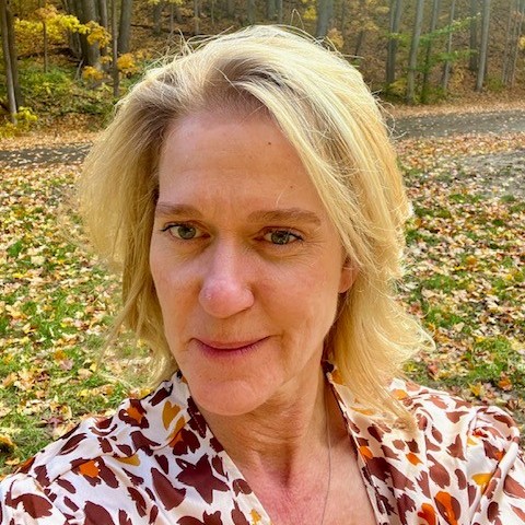 Person outdoors in autumn forest with fallen leaves.