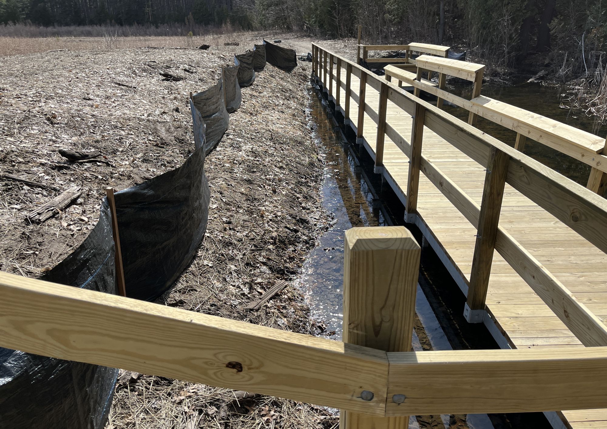 soil erosion Wooden boardwalk beside a silt fence in a forest.